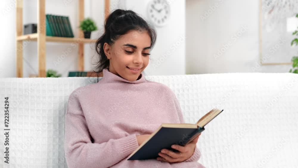 Young Arabic woman reading book at home, sitting alone on soft comfortable sofa, relax in weekend Young Arabic woman reading book at home, sitting alone on soft comfortable sofa, relax in weekend