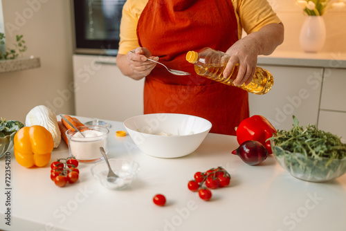 Woman seasons a vegetable salad while preparing food in the kitchen. Unrecognizable chef adds olive oil while preparing a vegetarian meal at home. Healthy eating concept. 