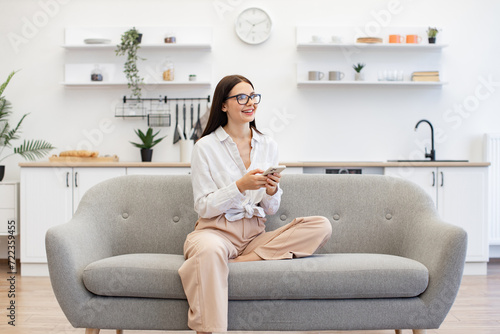 Free Download Happy young woman working remotely from home, typing on modern wireless cell phone. Relaxed lady sitting on comfy sofa and enjoying chatting with coworkers using smartphone on weekend. - GFXLoad