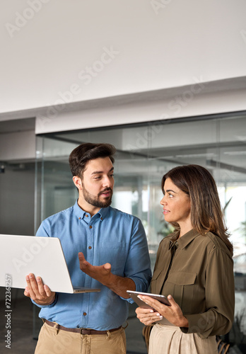 Two busy professional business people working in office with computer. Female executive manager talking to male colleague having conversation showing software online solution on laptop. Vertical.