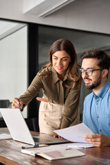 Professional mature business woman manager explaining corporate software elearning solutions helping young employee at work. Busy business people using laptop talking in office. Vertical shot.