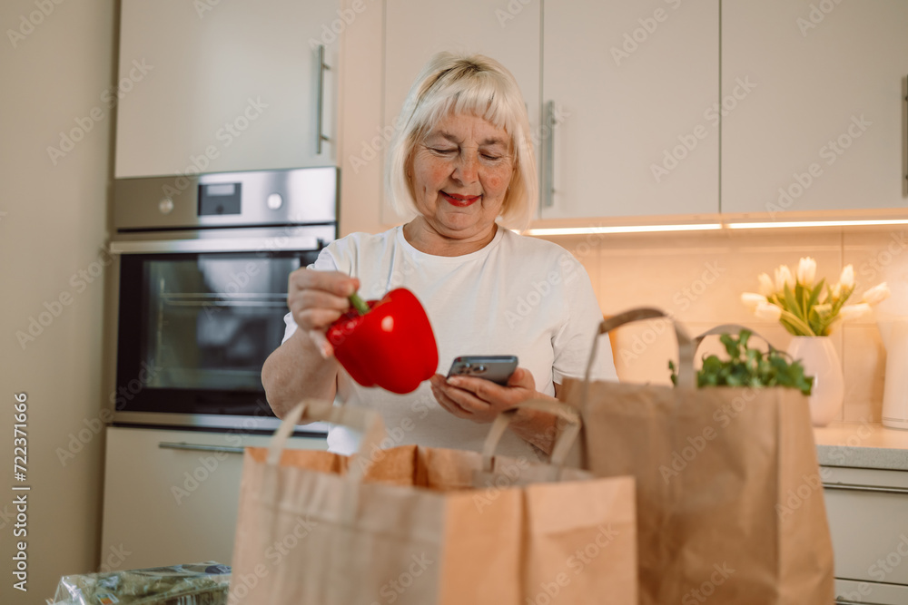 Happy lady unpacking groceries at home. Portrait of cheerful beautiful woman at kitchen table counter with bags full of apples, oranges, peppers, tomatoes, zucchinis, parsley from food market. High Happy lady unpacking groceries at home. Portrait of cheerful beautiful woman at kitchen table counter with bags full of apples, oranges, peppers, tomatoes, zucchinis, parsley from food market. High