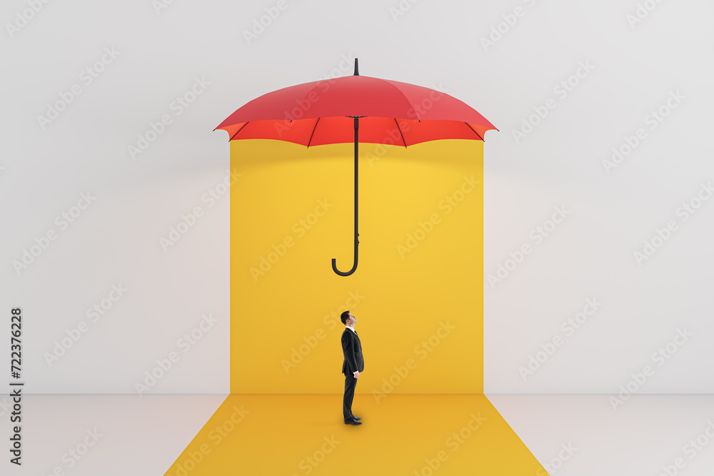 Side view of young businessman standing under red umbrella on yellow background. Protection and insurance concept. Side view of young businessman standing under red umbrella on yellow background. Protection and insurance concept.