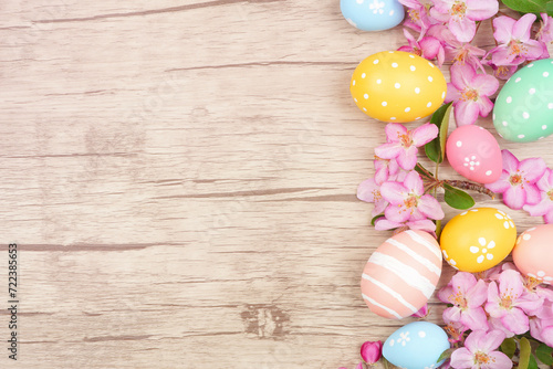 Easter eggs and cherry blossom flowers. Above view side border against a light wood background. Copy space.