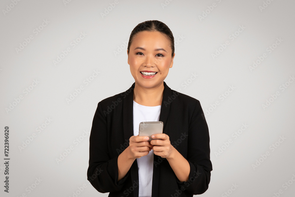 Smiling Asian businesswoman in a stylish black blazer intently using a smartphone