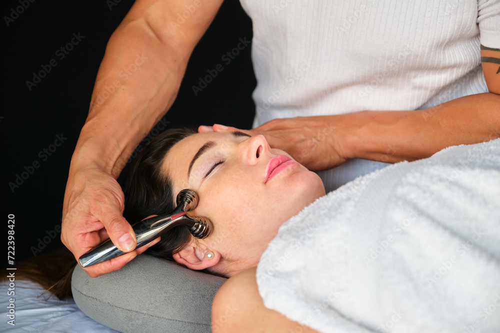 Woman getting face massage with a facial cooling metal roller. Professional skin care treatment. Woman getting face massage with a facial cooling metal roller. Professional skin care treatment.