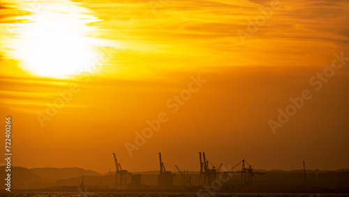 Panoramic view of orange sunset sunrise sky and silhouettes of port cranes in the Mediterranean port of Alicante, Spain.