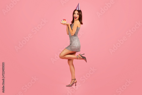 Excited young woman in a sparkling silver dress, holding a birthday cupcake with a candle