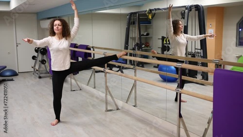 Woman put one leg on railing and squat on one leg with raised hands photo