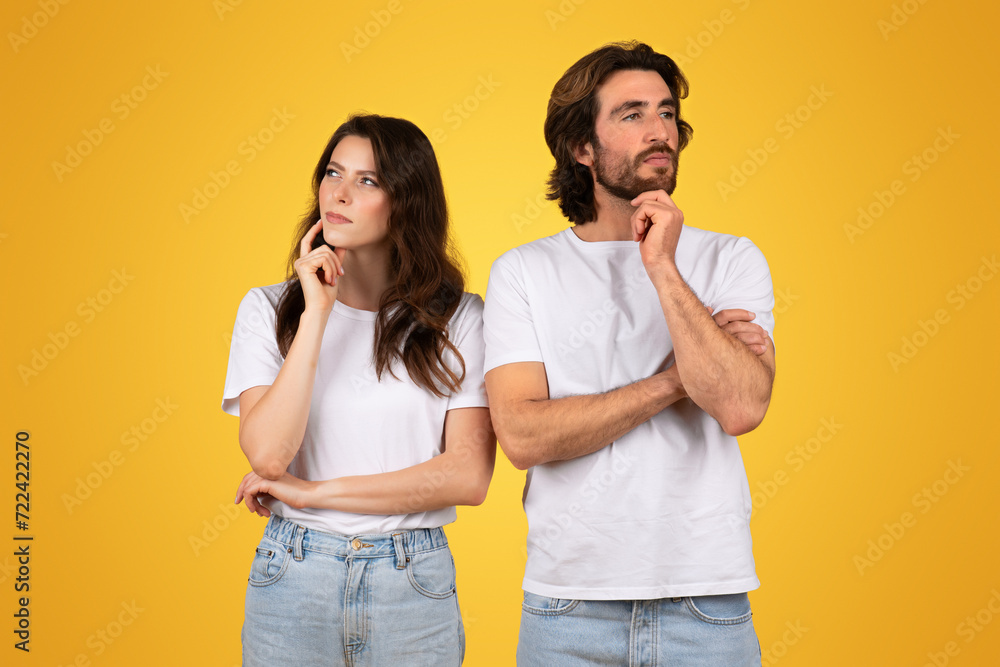 Pensive couple in white t-shirts and blue jeans, standing back-to-back with thoughtful expressions Pensive couple in white t-shirts and blue jeans, standing back-to-back with thoughtful expressions