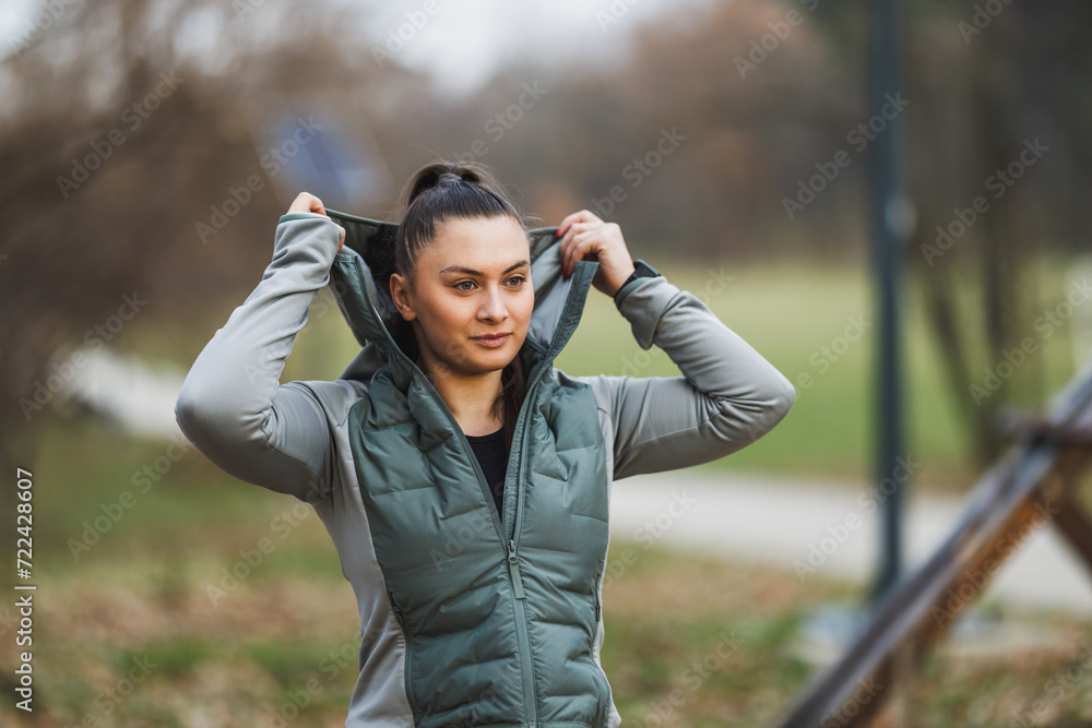 Woman in Jacket Holding Hoodie Over Head And Preparing for Outdoor Training Woman in Jacket Holding Hoodie Over Head And Preparing for Outdoor Training