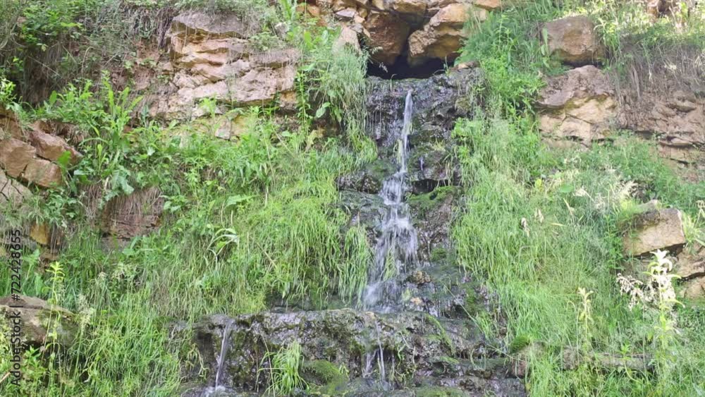 Waterfall from hole on wall treed with green grass at summer day. Waterfall from hole on wall treed with green grass at summer day.