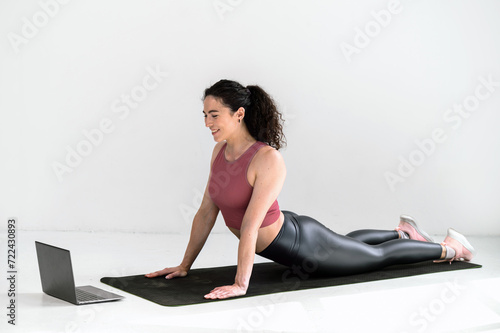 Smiling young woman doing stretching at home while using notebook
