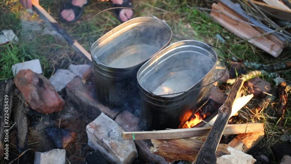Two pots with water on bricks on campfire and hand laying firewood