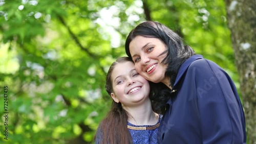 Mother and daughter cuddle, touch cheeks and smile in park.