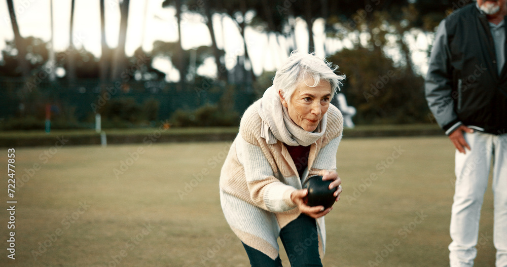 Fototapeta premium Senior woman, bowling and park on grass for sport, fitness and games for competition, health or fun. Elderly people, metal ball and lawn for contest, funny laugh or workout with blowing for good luck
