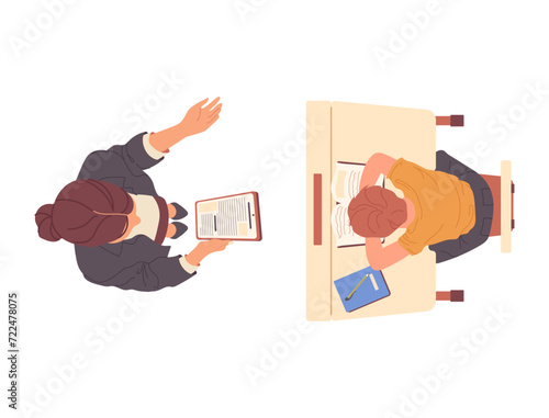 Woman teacher reading dictation for schoolboy child writing in copybook sitting at desk top view