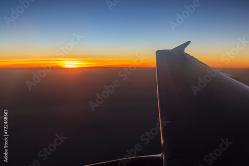 Flying above the clouds. Scenic view of sun, cloudy sky and airplane wing at sunset.