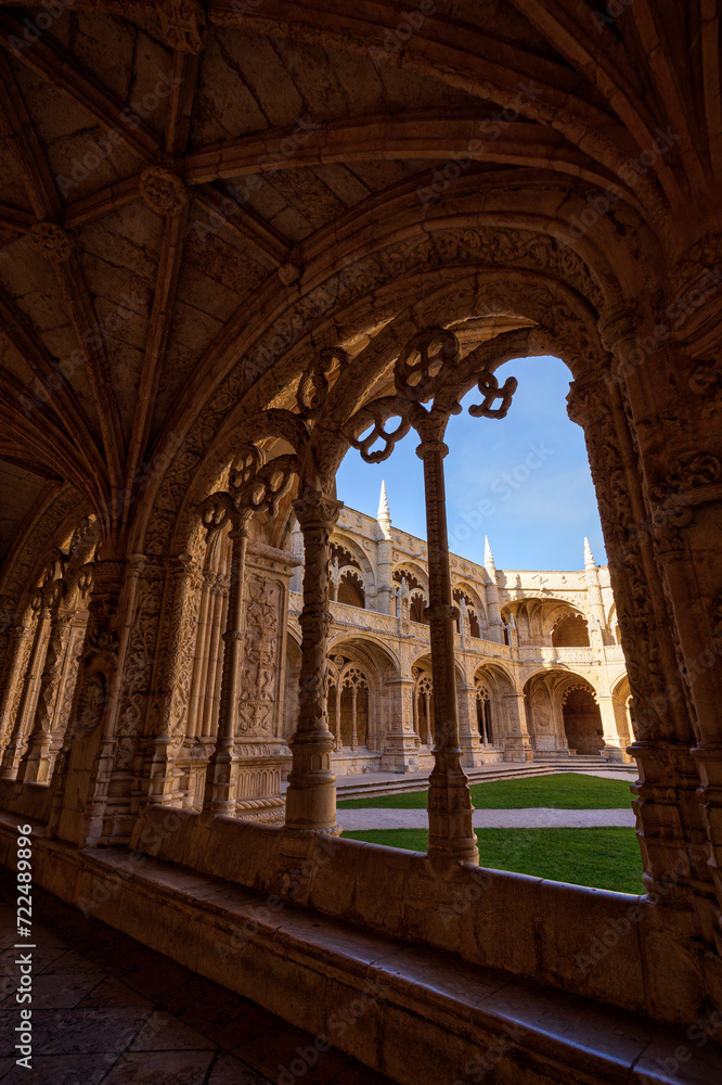Empty inner courtyard viewed through an ornate window at the historic Manueline style Mosteiro dos Jeronimos (Jeronimos Monastery) in Belem, Lisbon, Portugal, on a sunny day.