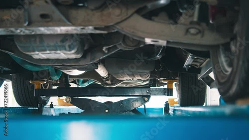 An automobile is poised on a pneumatic lift in a car service station. The lift's arms securely hold the car, providing a clear view of the vehicle's exhaust system, chassis, and tires, indicative of a