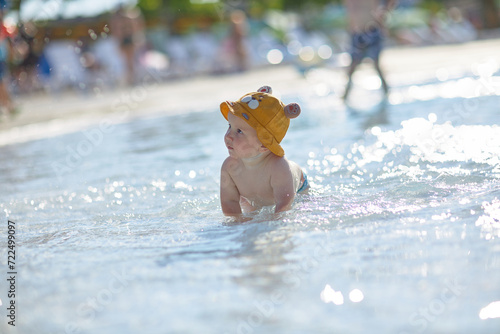 a little half a year old, a baby baby crawling on the water, smiling, outdoors, in a panama hat, in diapers, in the sun at the resort.
