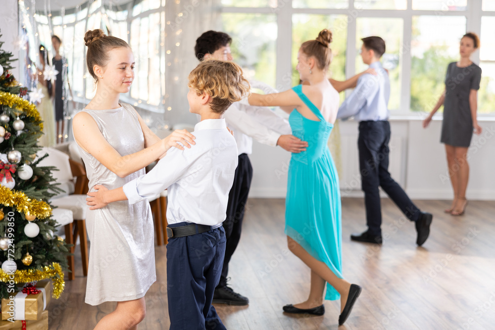 Positive teen boy and girl are dancing classic version of waltz in couple during lesson at studio in New Year atmosphere. Leisure activities and physical activity for positive children.