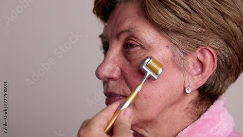 portrait head shoot of beautiful elder woman using derma roller with needles for facial rejuvenation, face anti aging wrinkle procedures at home. smiling female granny photo