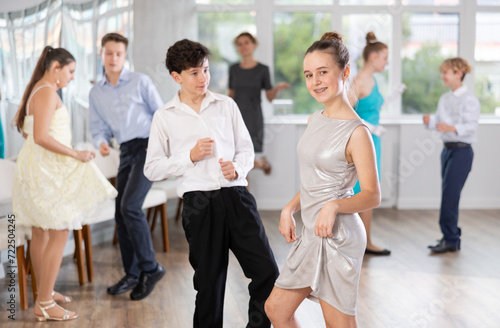 Group of happy teenagers in festive clothes dancing foxtrot in dance studio