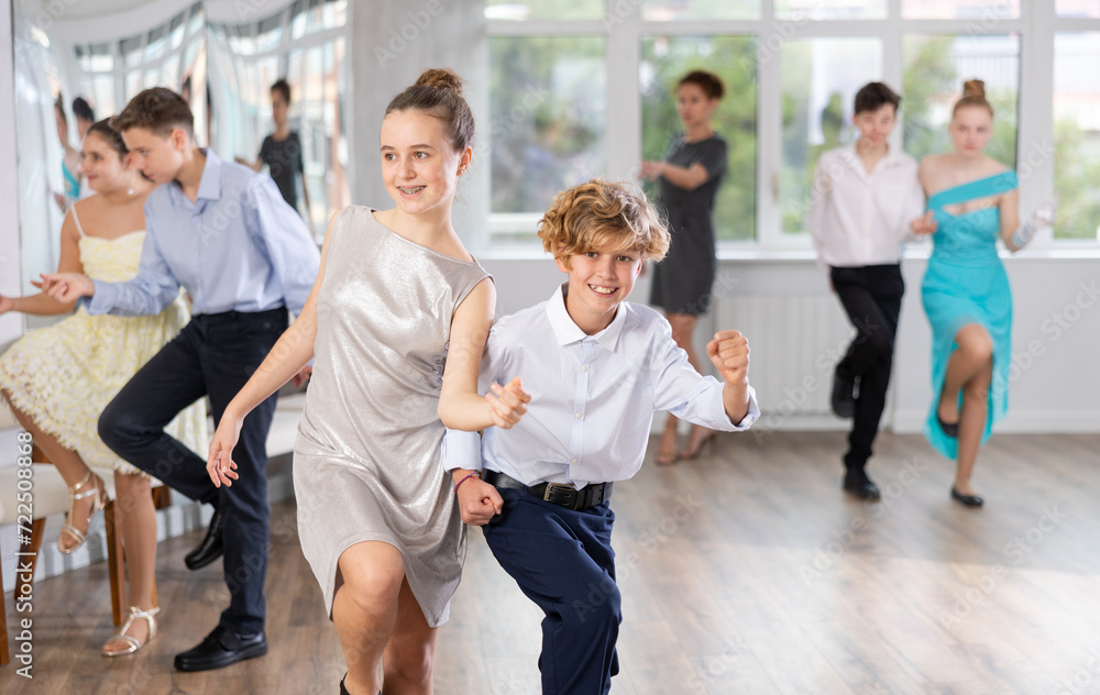 Group of joyful active young dancers practicing in bright dance studio with female instructor in background