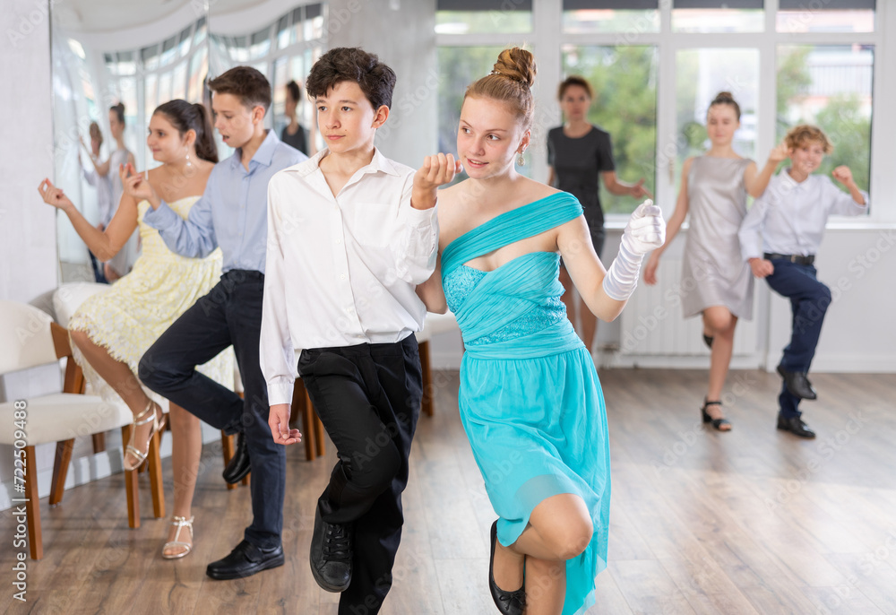 Enthusiastic adolescent partners, girl and boy confidently performing routine in pair in dance studio with group of peers ..