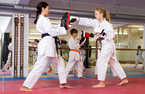 Young girls and boys in boxing gloves exercising jabs during group karate training. Female trainer with focus mitts teaching girl in foreground.