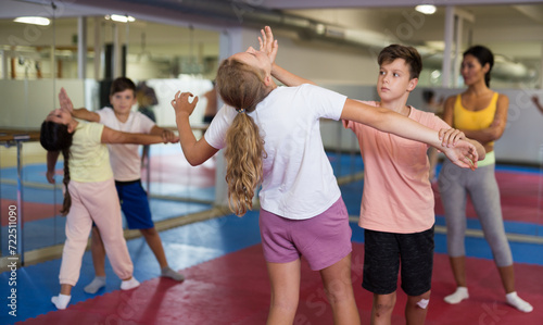 Positive kids in pair exercising self-defense movements during group class with female coach