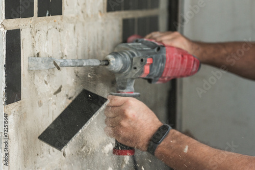 Builder with a puncher dismantles old tiles from a concrete wall photo