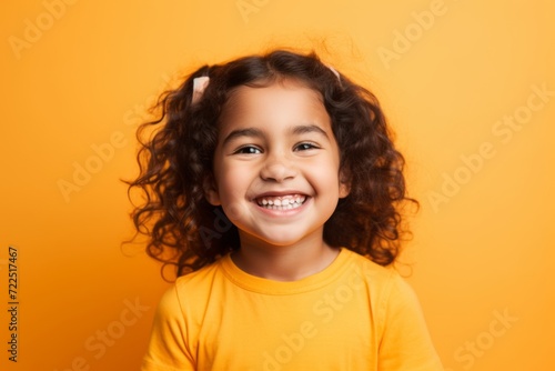 Portrait of a smiling little girl with curly hair over yellow background © Inigo