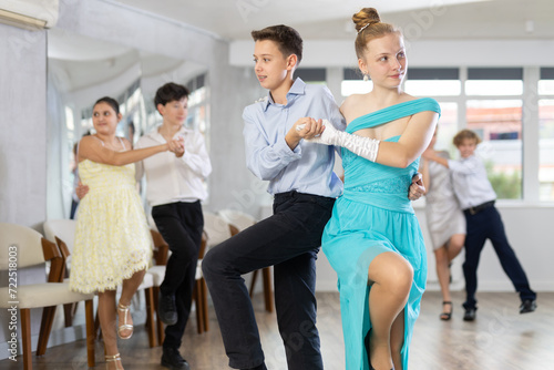 Enthusiastic adolescent partners, girl and boy confidently performing routine in pair in dance studio with group of peers ..