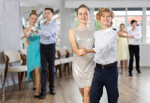 With unhurried music, teen boy and girl in couple spins to rhythm of tango during lesson for novice students. Classes in mini-groups for those who want to learn dancing photo