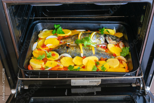 View of a delicious raw mackerel with potatoes and tomato, onion, lemon and spices in a dish prepared to put in the oven photo