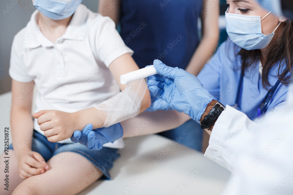Close-up shows an injury on arm of patient being meticulously wrapped with sterile bandage by multicultural medical personnel. Photo focus on a youngster who is being treated by a doctor and a nurse.