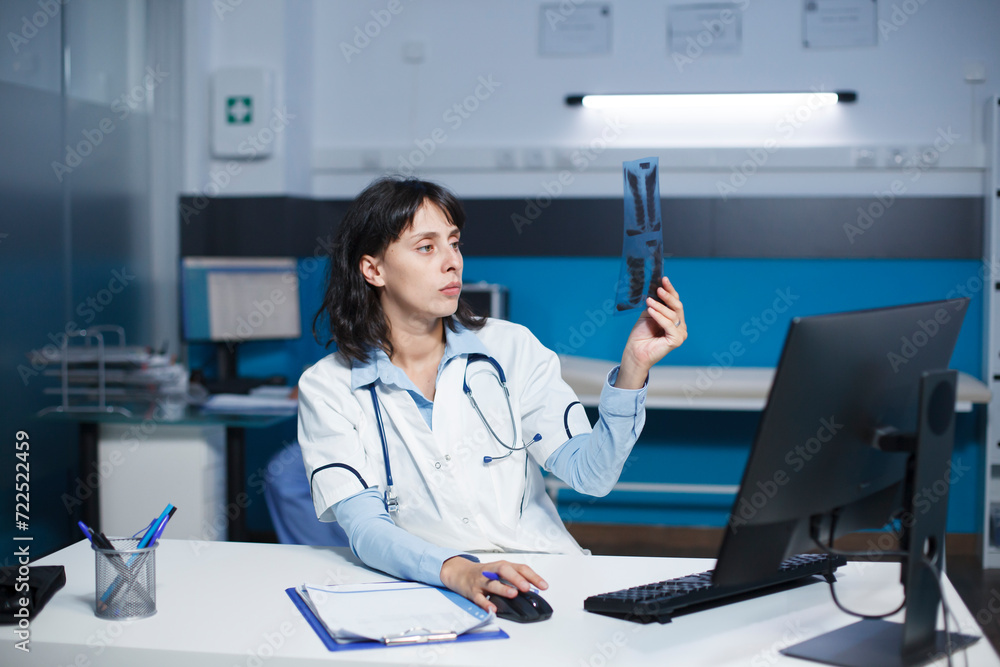 Dedicated doctor examining a CT scan of a patient, taking notes on desktop computer. The image shows caucasian female healthcare professional inspecting a chest X-ray image of an individual. Dedicated doctor examining a CT scan of a patient, taking notes on desktop computer. The image shows caucasian female healthcare professional inspecting a chest X-ray image of an individual.