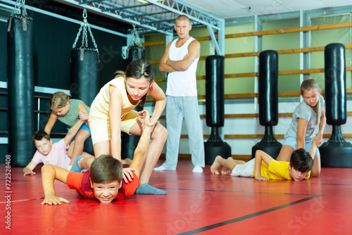 Sportive preteen kids practicing in pair self-protection in class with teacher