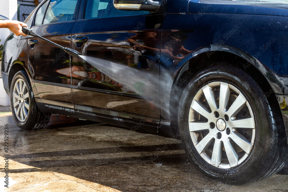 Man washing a car wheel rim with high pressure power washer gun at the carwash.