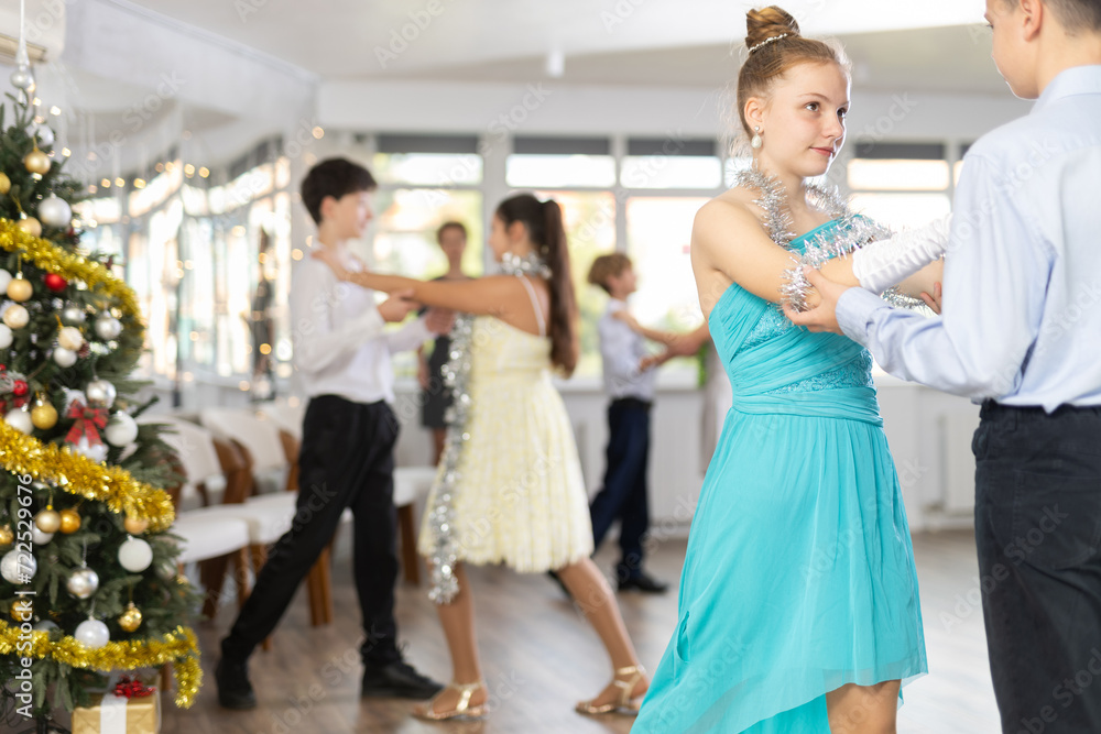 Fototapeta premium With unhurried music, teen boy and girl in couple spins to rhythm of tango during lesson for novice students in Christmas atmosphere. Classes in mini-groups for those who want to learn dancing