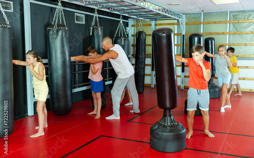 Boxing instructor and young preteen children practicing blows on the punching bags during training at gym © JackF