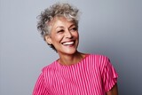Portrait of a happy senior woman laughing against a grey background.
