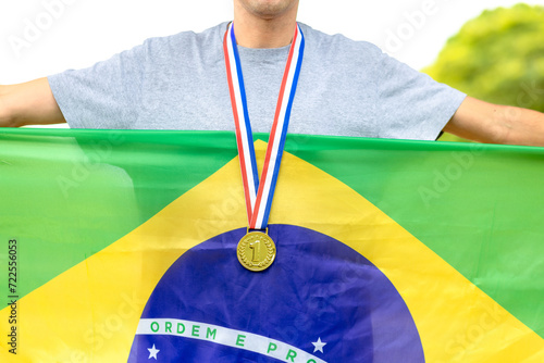 Atleta masculino brasileiro exibindo com orgulho a sua medalha de ouro, simbolizando a vitória. Ele segura a bandeira do Brasil,  para demonstrar o orgulho nacional durante eventos esportivos. photo