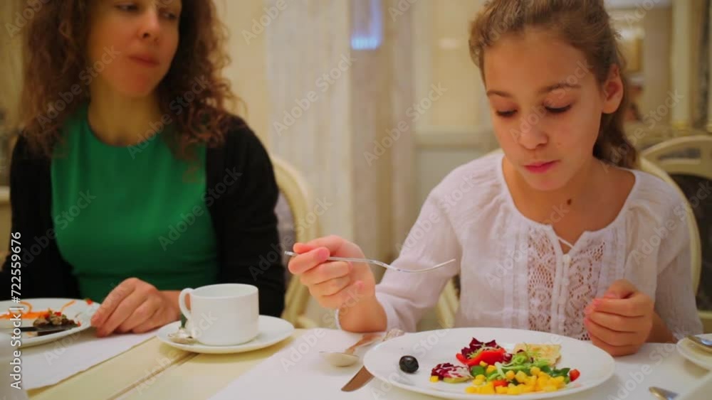 Mother and daughter eat vegetables from plates during dinner Mother and daughter eat vegetables from plates during dinner