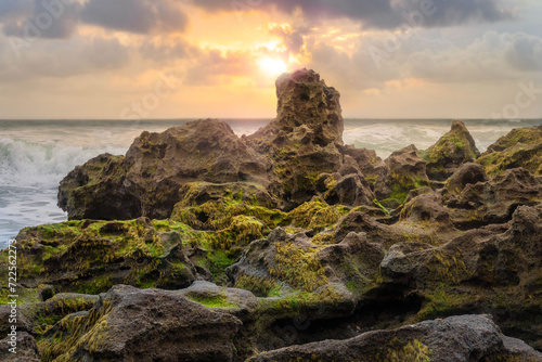 Sunlit mossy rock formations on a rugged beach at sunset, a captivating scene for eco-tourism and natural history publications.