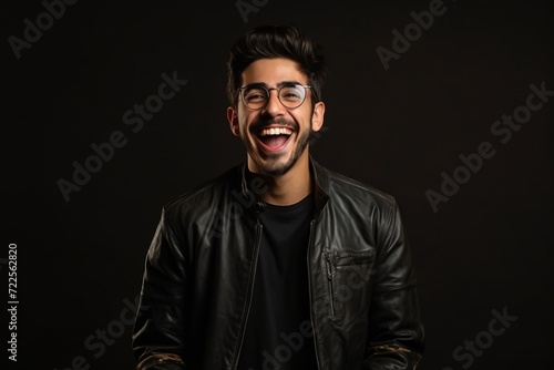 Portrait of a happy young man in leather jacket and eyeglasses over black background