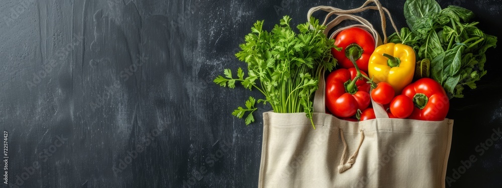 Reusable fabric bag filled with fresh red and yellow bell peppers and lush green herbs on a dark background. Reusable fabric bag filled with fresh red and yellow bell peppers and lush green herbs on a dark background.