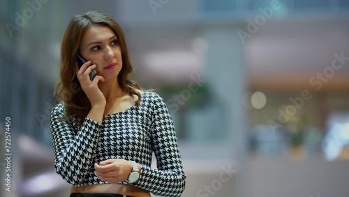 Woman in blouse talks by smart-phone in hall of business center photo